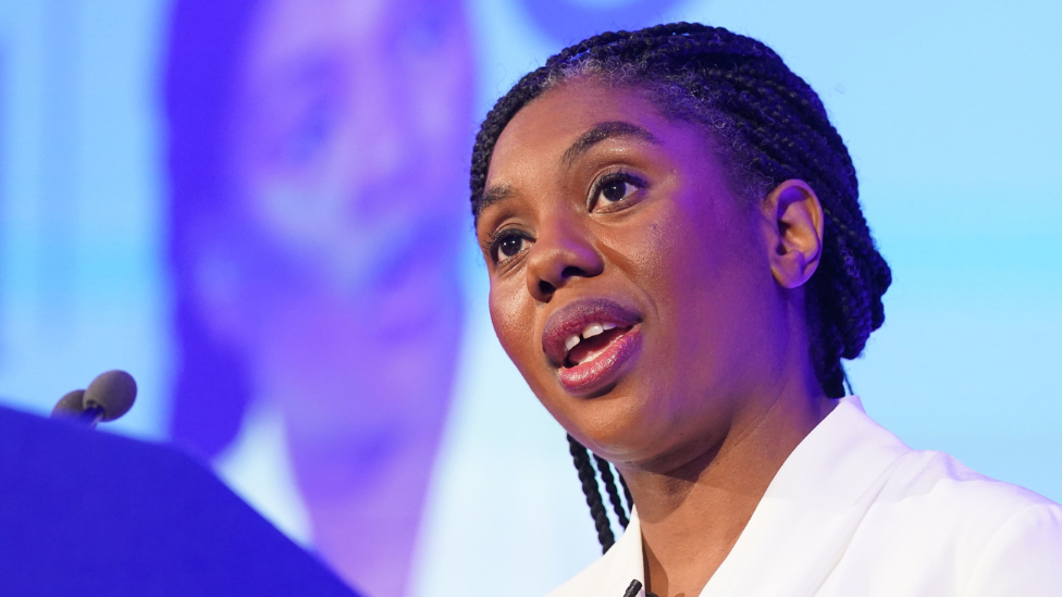 Kemi Badenoch speaking at a podium - the image is close up on her head and shoulders, she is in the middle of speaking. She is wearing a white top.