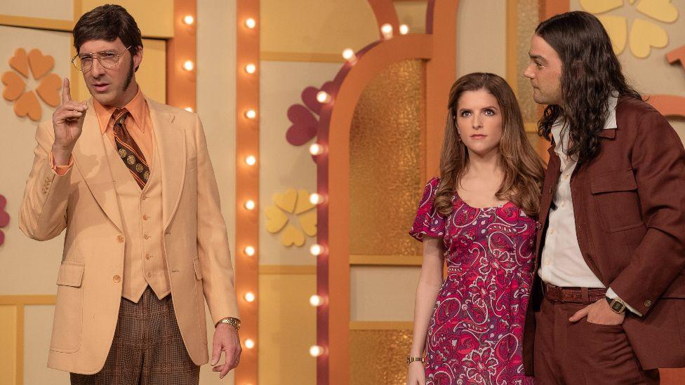 Tony Hale in a beige and brown 70s suit, Anna Kendrick in a red paisley dress and Daniel Zovatto in a brown 70s suit in Netflix's Woman of the Hour