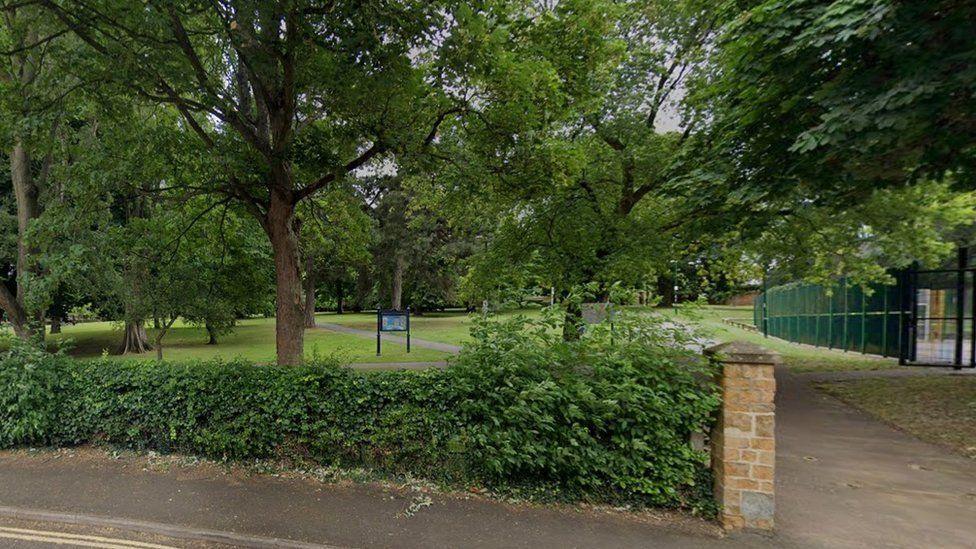 Hedging and path lead into the park with dense trees and lawn areas