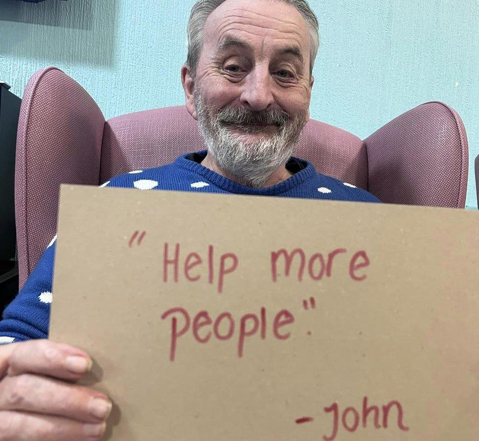 A resident holds up a sign reading 'Help more people'