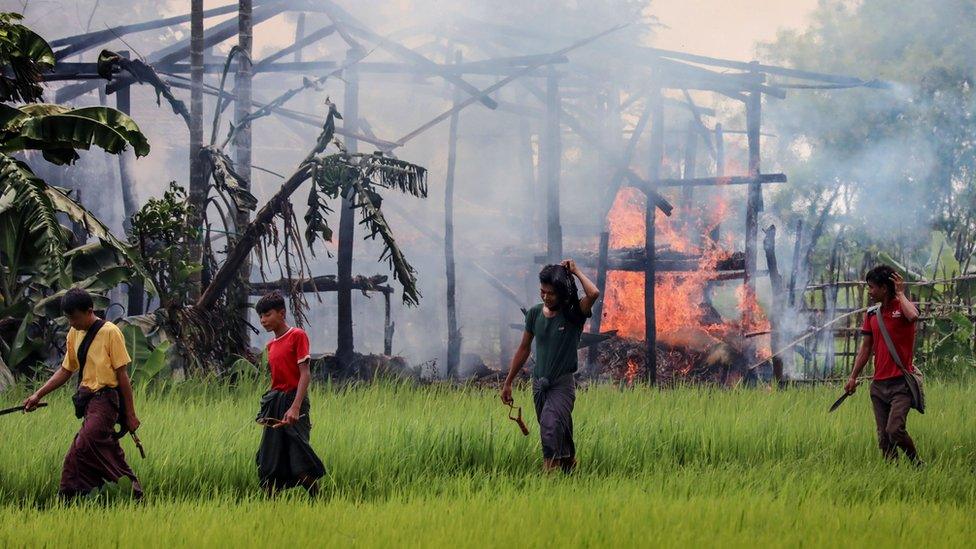 Armed men walk past burning homes in Rakhine state