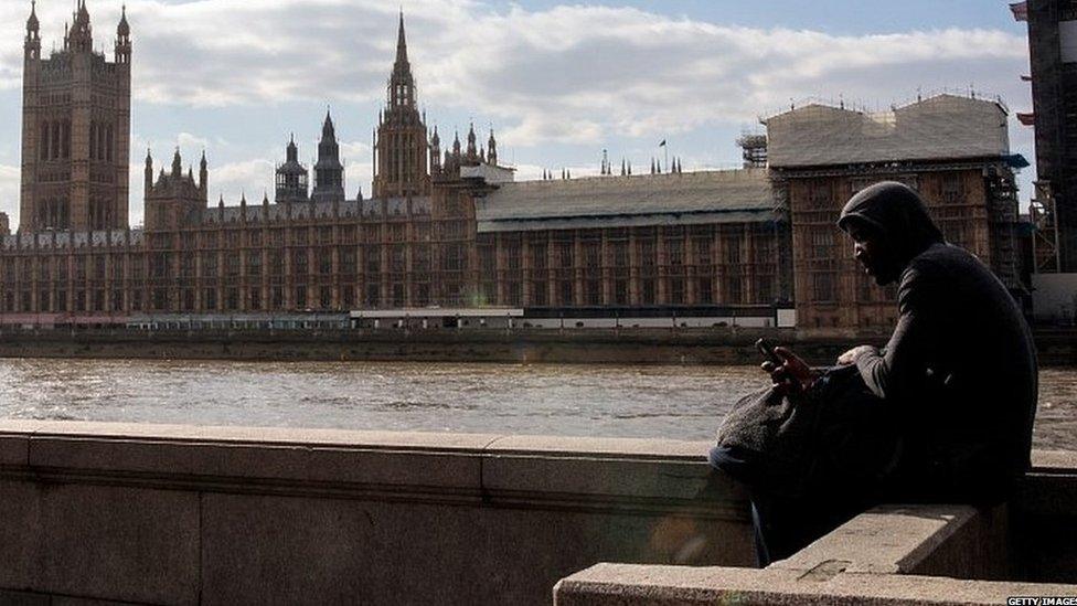 Man sits on the bank of the River Thames opposite the Houses of Parliament