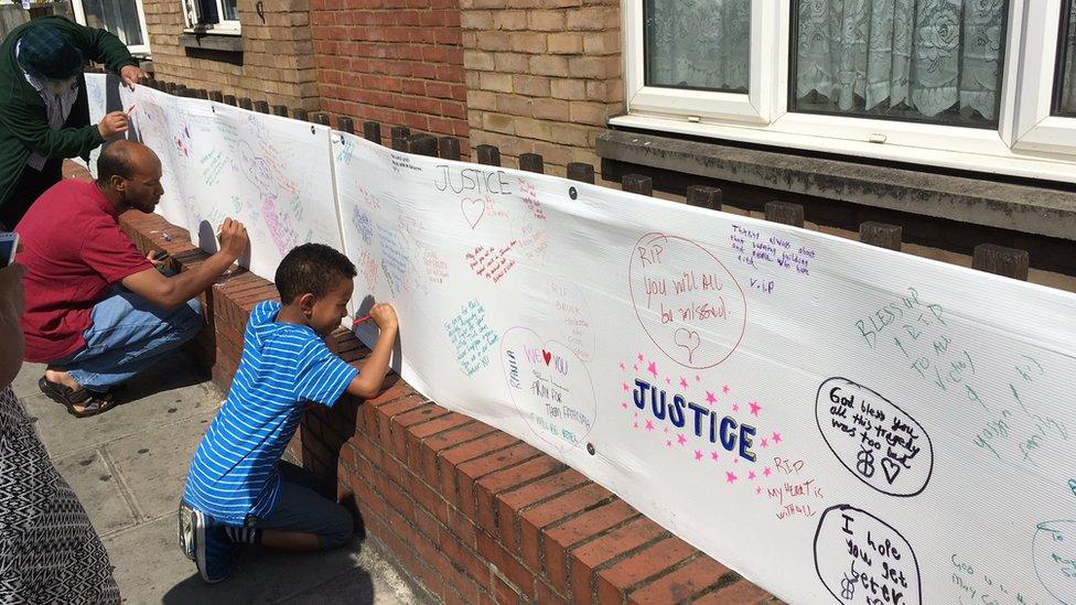 people including a young boy signing a wall of condolence messages