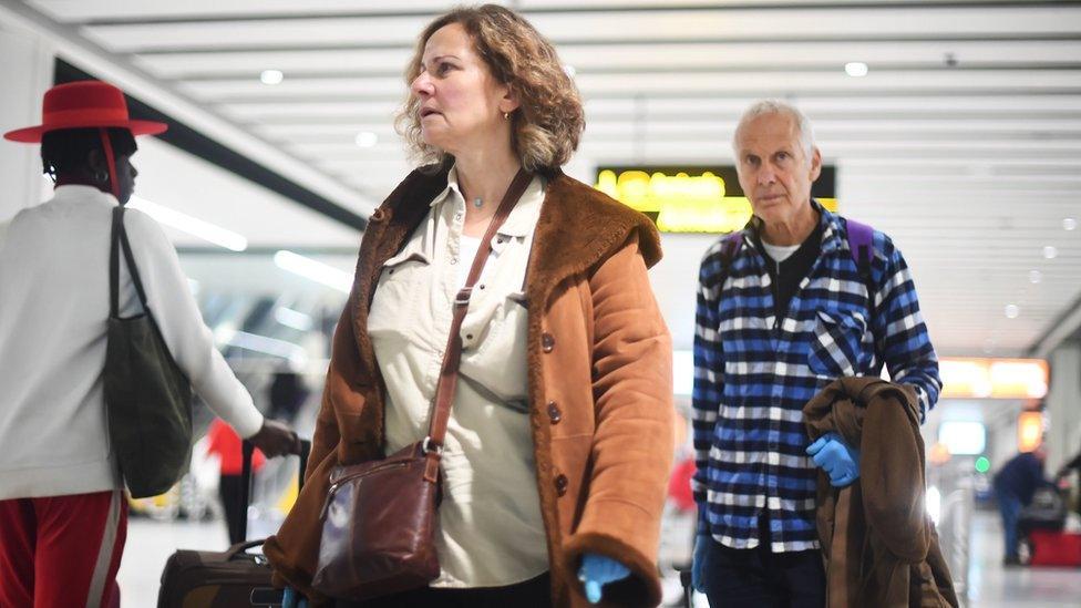 A couple walking through Gatwick Airport wearing latex gloves