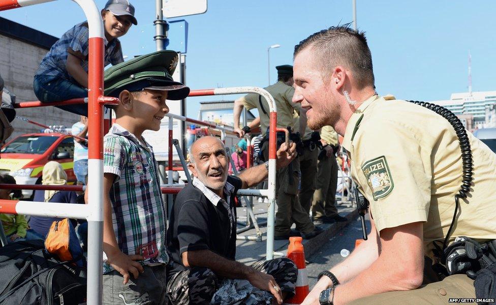 German police officer and a migrant boy joke with the officer"s cap while migrants wait for a bus after their arrival at the main train station in Munich, southern Germany, September 1, 2015.