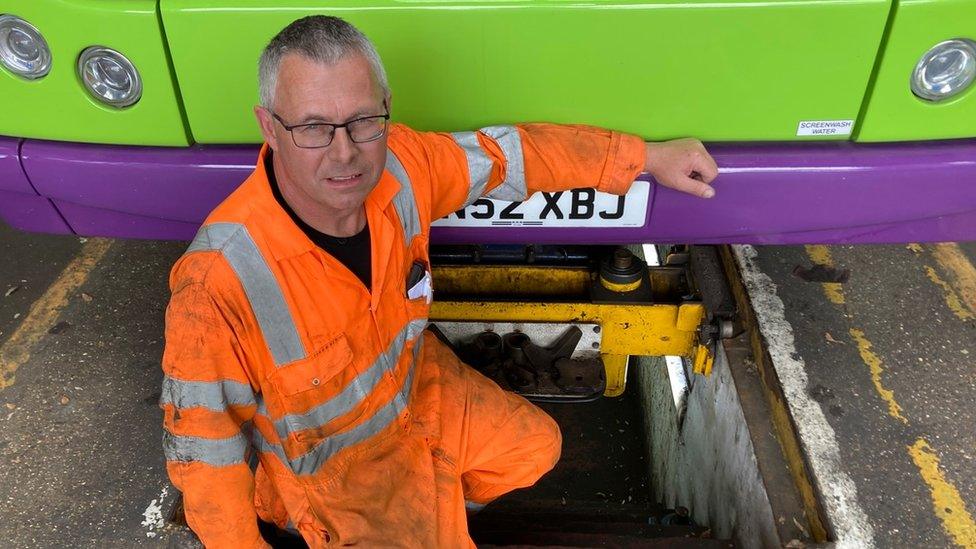 Brian Reach wearing hi-vis and standing in a mechanic's pit in front of a bus