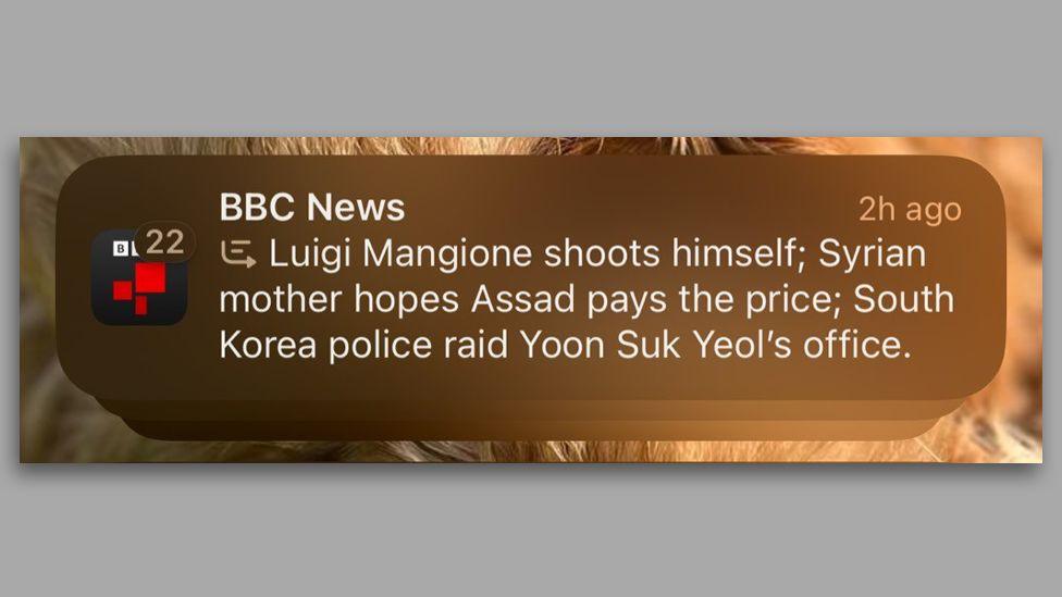 A zoomed-in phone screenshot of the misleading BBC notification from an iPhone. It reads: "BBC News, Luigi Mangione shoots himself; Syrian mother hopes Assad pays the price; South Korea police raid Yoon Suk Yeol's office".