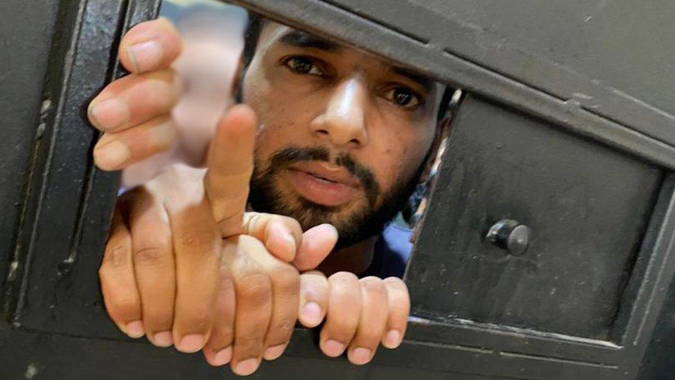 Man with a beard looks through a small window in a metal door