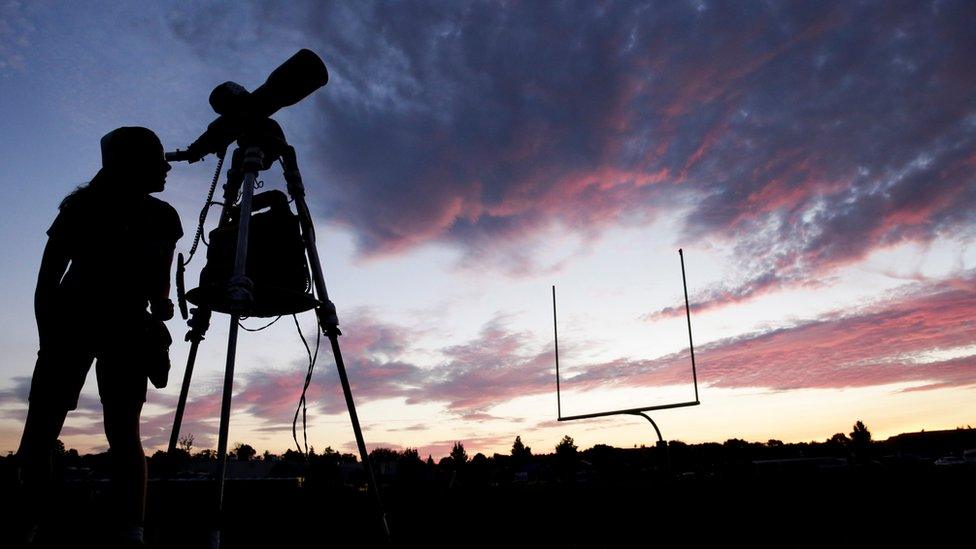 A woman looks through a telescope on a high school football field ahead of the eclipse.