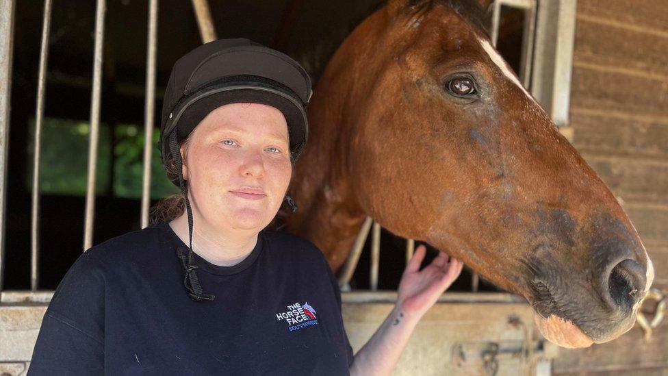 A woman and a brown horse in a stable