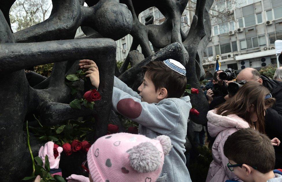 A child lays roses at the Holocaust Memorial monument in Thessaloniki