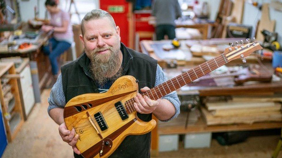 Gavin Pond who runs the workshops holding an electric guitar made of wood