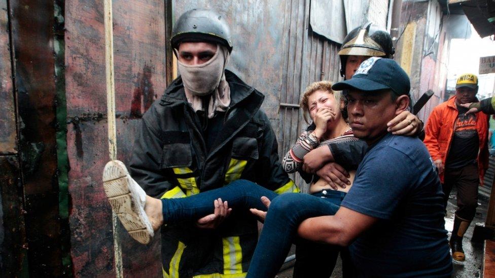 Firefighters help to evacuate a woman affected by smoke from a fire at the oriental market