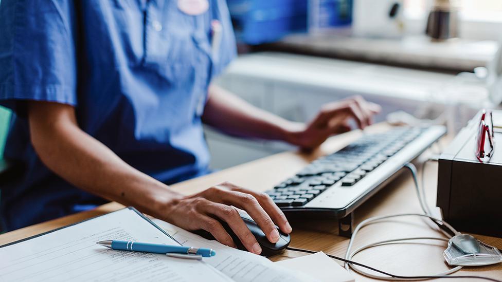 Stock photo showing a doctor using a computer at desk with hand on mouse and keyboard