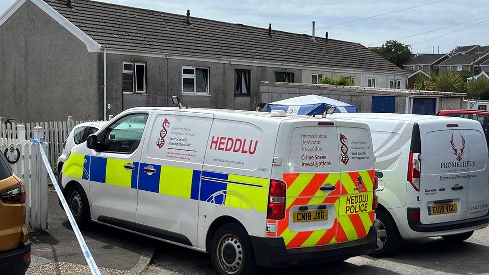 Police van inside police tape parked in front of home with burnt out windows