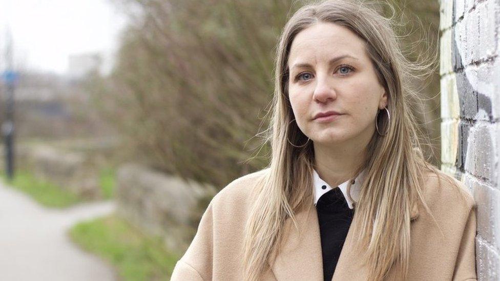 Sarah stands outside by a public footpath, by a wall