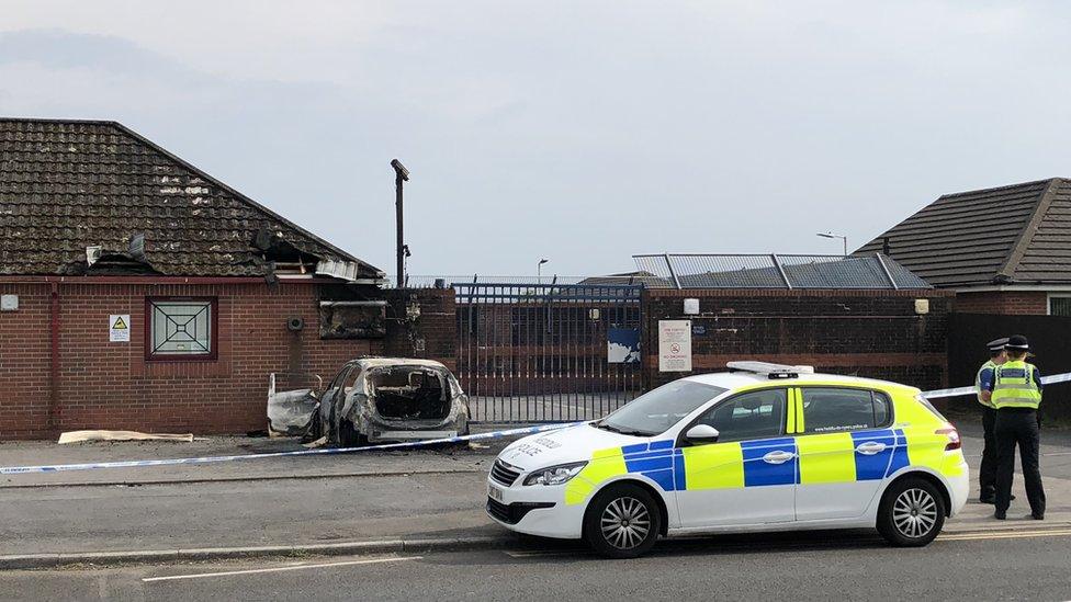 A burned out police car , two police officers and police cordon