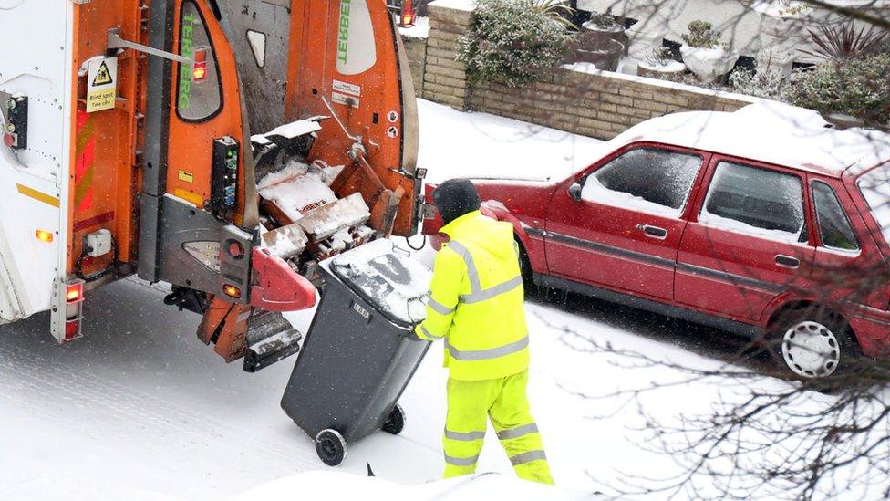 A binman putting a bin in a lorry in the snow