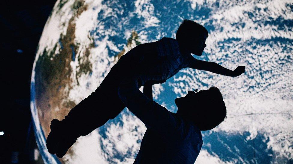 A young boy is lifted up in front of an Earth model