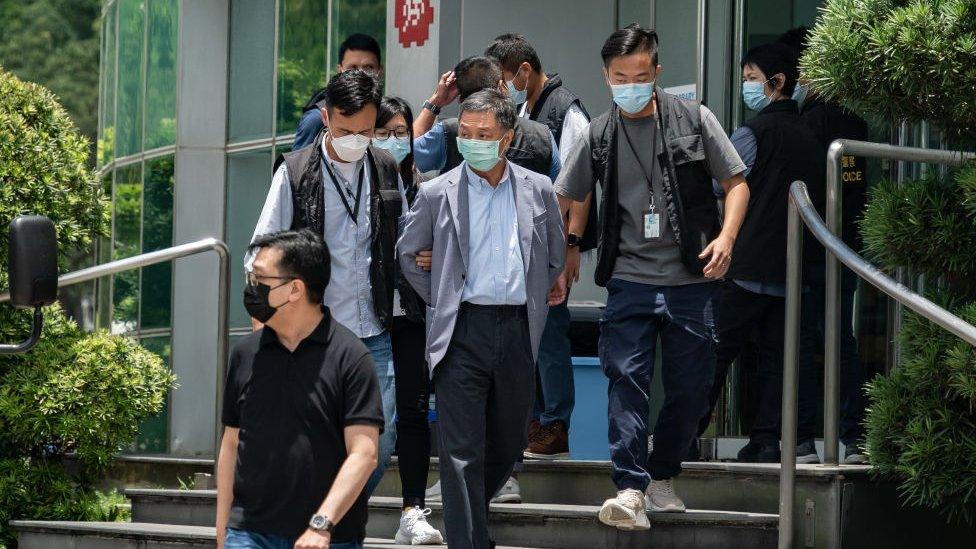 Chief Operations Officer Chow Tat Kuen (C) is escorted by police from the headquarters of the Apple Daily newspaper