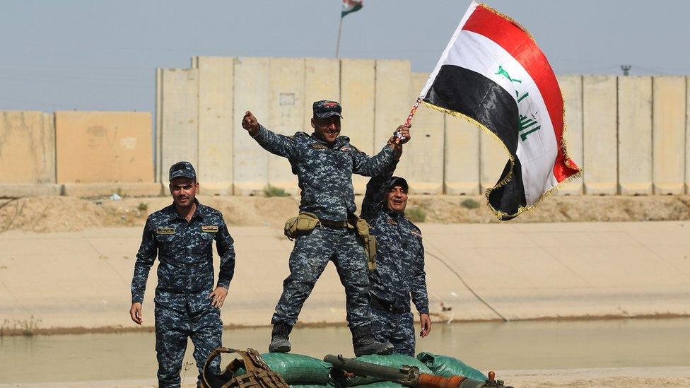 Iraqi forces pose with a national flag as they stand on a river bank across from Kurdish peshmerga positions on October 14, 2017, on the southern outskirts of Kirkuk.