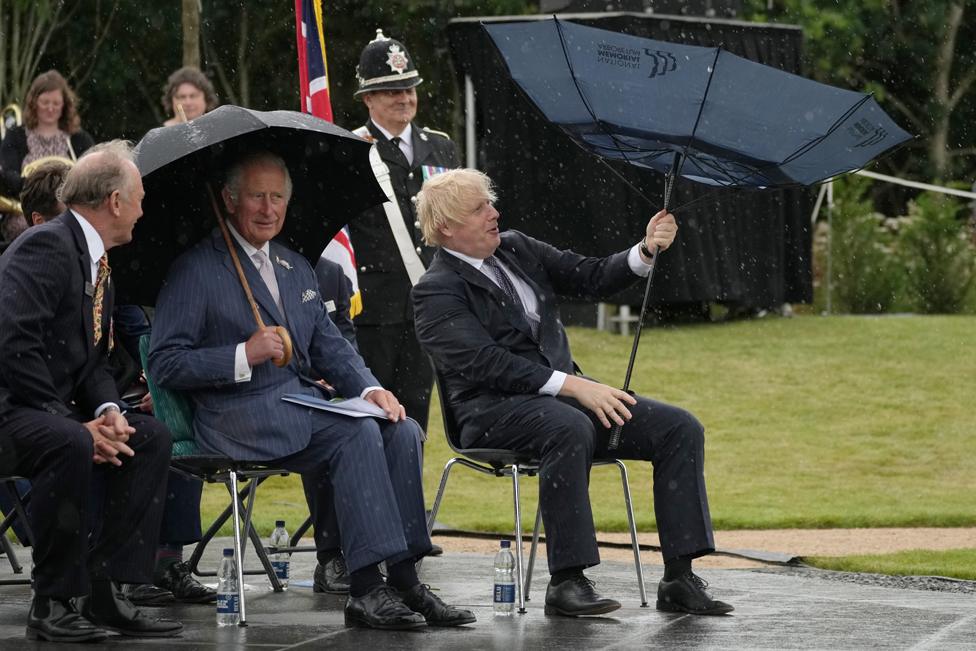 Prince Charles, Prince of Wales looks on as British Prime Minister, Boris Johnson opens his umbrella at The National Memorial Arboretum on 28 July 2021 in Stafford, England.