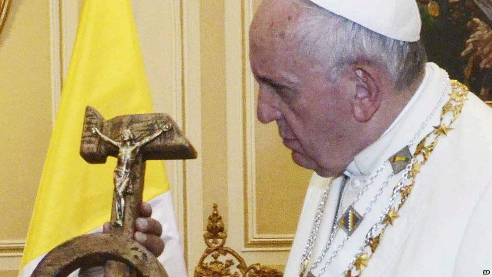 Pope Francis reacts as he is given a crucifix shaped as a hammer and sickle