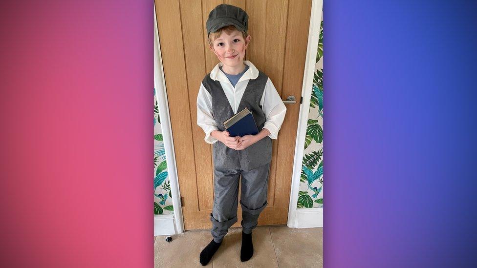 boy wearing a cap and waistcoat holding a book with dirt on his cheeks