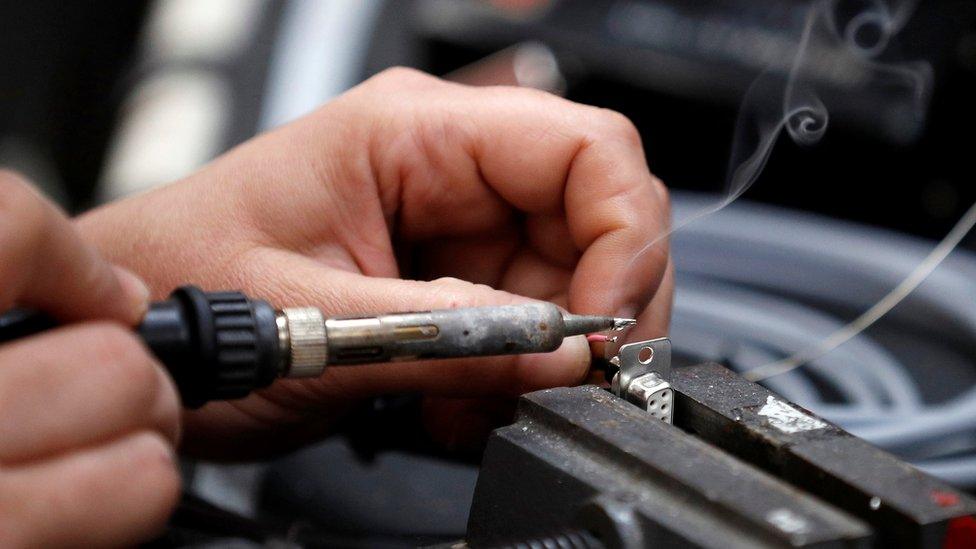 A worker solders electrical wire to a component on the factory floor of PP Control and Automation near Cannock