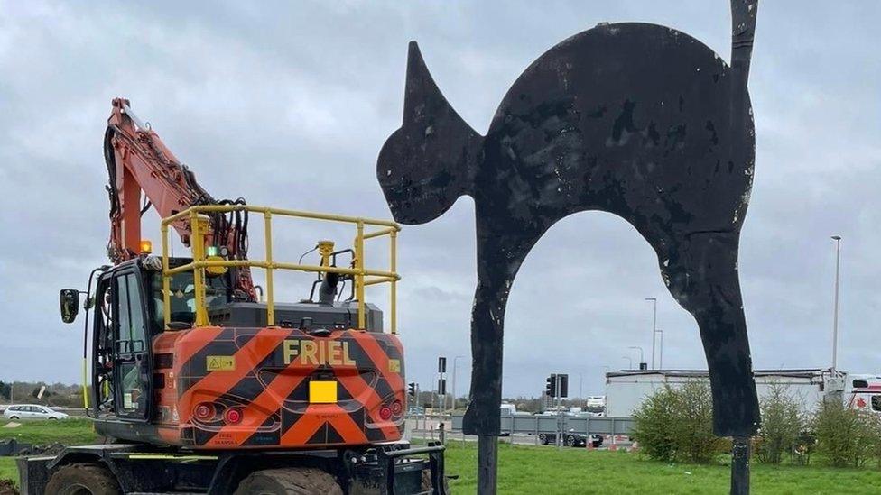 A sculpture of a large black cat in the middle of a roundabout