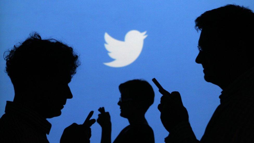 People holding mobile phones are silhouetted against a backdrop projected with the Twitter logo in this illustration picture taken in Warsaw September 27, 2013.