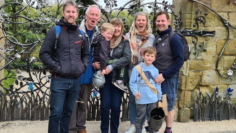 Three men, two women and two children stand in a group shot smiling at the camera