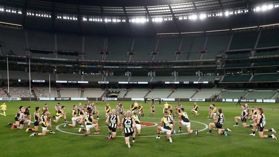 Players from the Collingwood and Richmond AFL teams take a knee prior to a match in June 2020 as a gesture of support for the Black Lives Matter movement