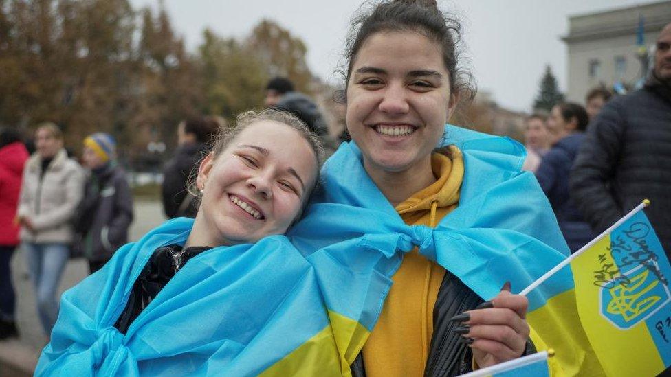 Two smiling women wearing Ukrainian flags celebrating in Kherson, after the city was liberated from Russian occupation