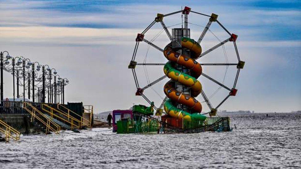 A slide and Ferris wheel are surrounded by high tide and water.