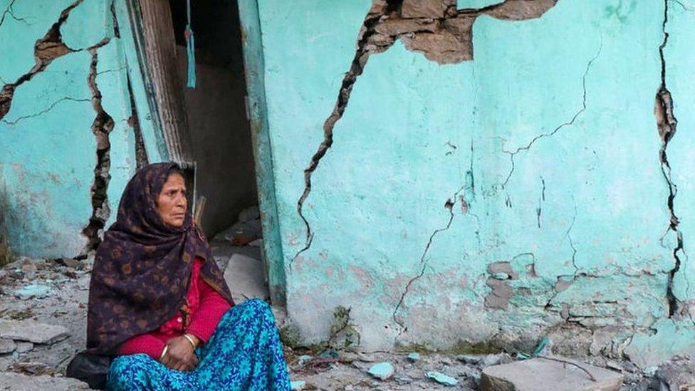 A woman sits beside a cracked wall of her house at Joshimath in Chamoli district of India's Uttarakhand state on January 10, 2023.