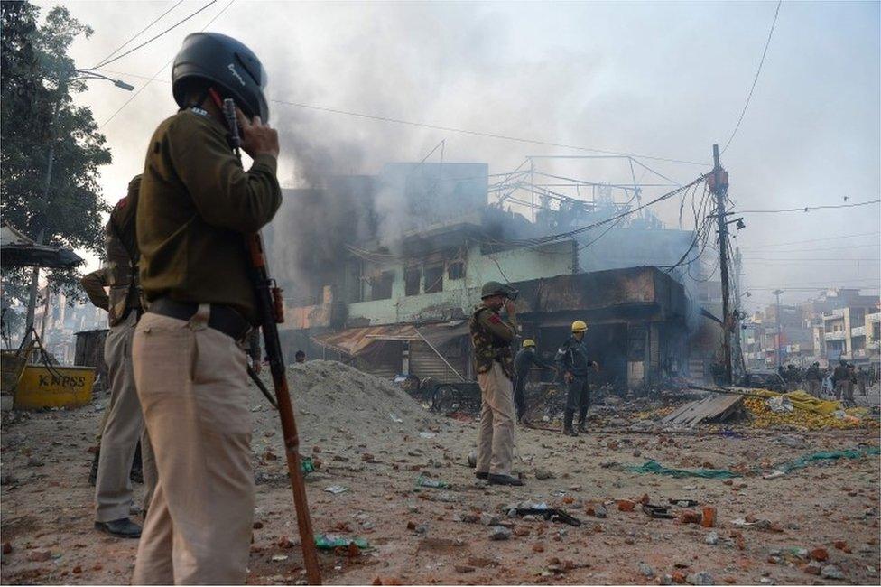 Policemen stand along a road scattered with stones as smoke billows from buildings following clashes between supporters and opponents of a new citizenship law, at Bhajanpura area of New Delhi on February 24, 2020