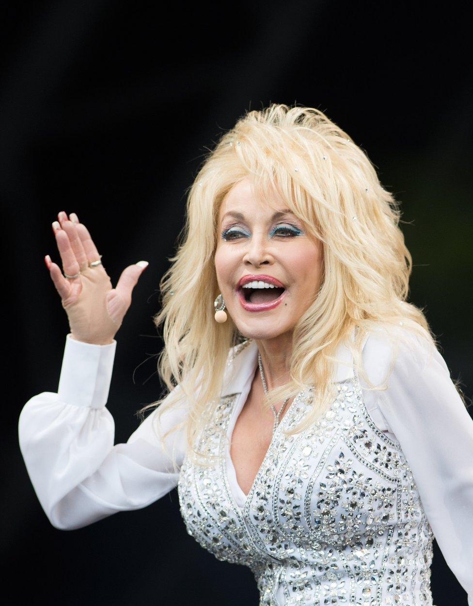 Dolly Parton holds her hand up to the audience