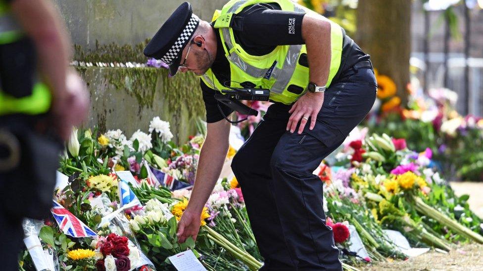 A police officer places flowers on behalf of a member of the public in the garden area outside the Palace of Holyroodhouse