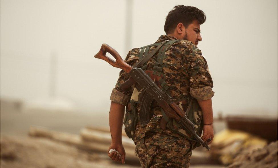 A member of the Kurdish People's Protection Units (YPG) walks with a Kalashnikov assault rifle slung behind his back in the town of al-Karamah, 26km from Raqqa, on 10 May 2017