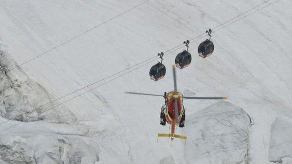 An EC-135 helicopter operated by French rescuers hovers near three cable cars suspended above Mont Blanc (09 September 2016)