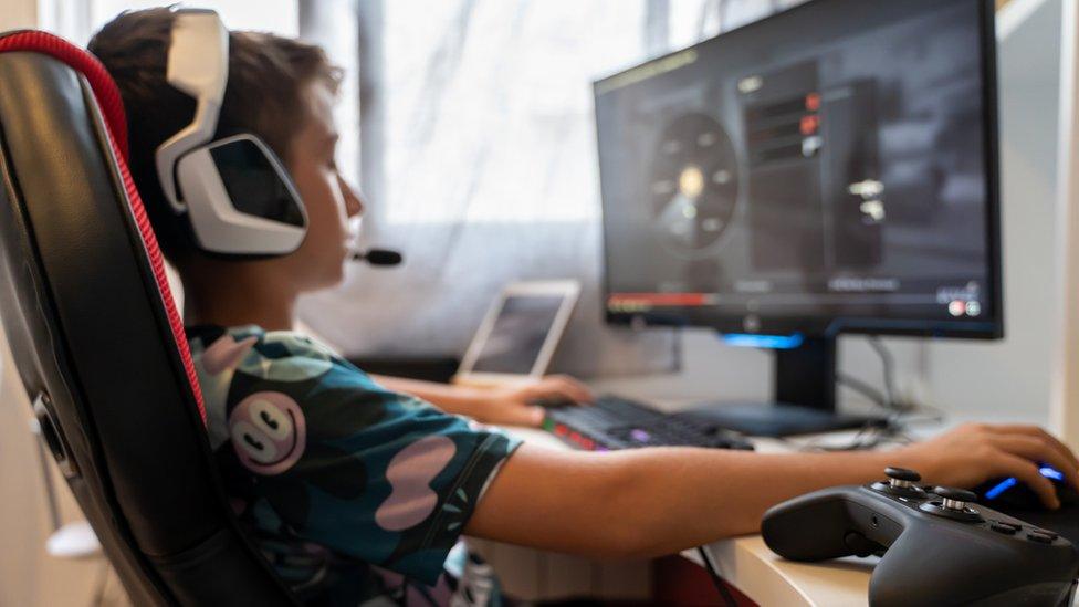 teenager sitting in an armchair in front of a computer playing with the mouse while wearing helmets