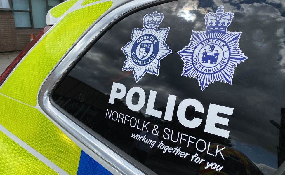 A police car with the badges for both Norfolk and Suffolk police forces on the window