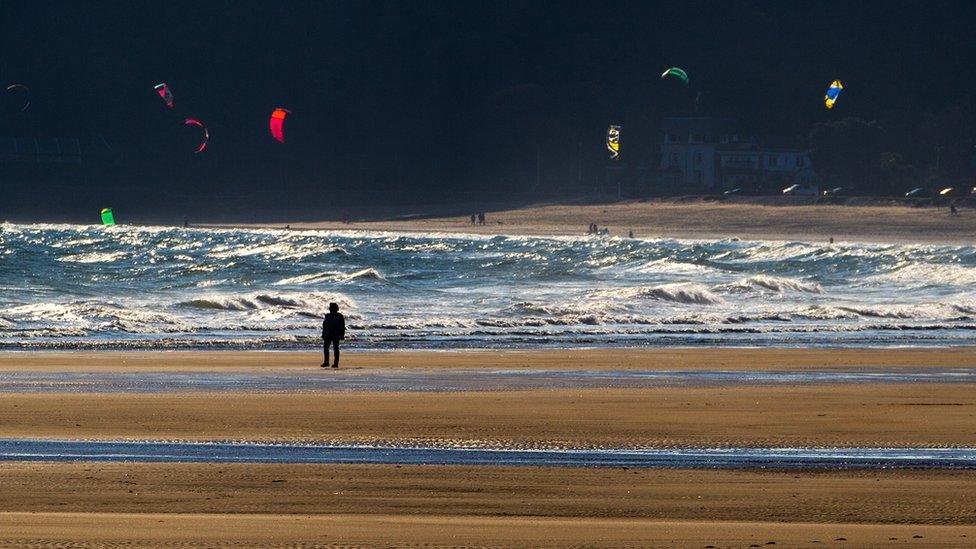 A lone walker looks on at the kite surfers on Oxwich Bay, Gower, taken by John Minopoli