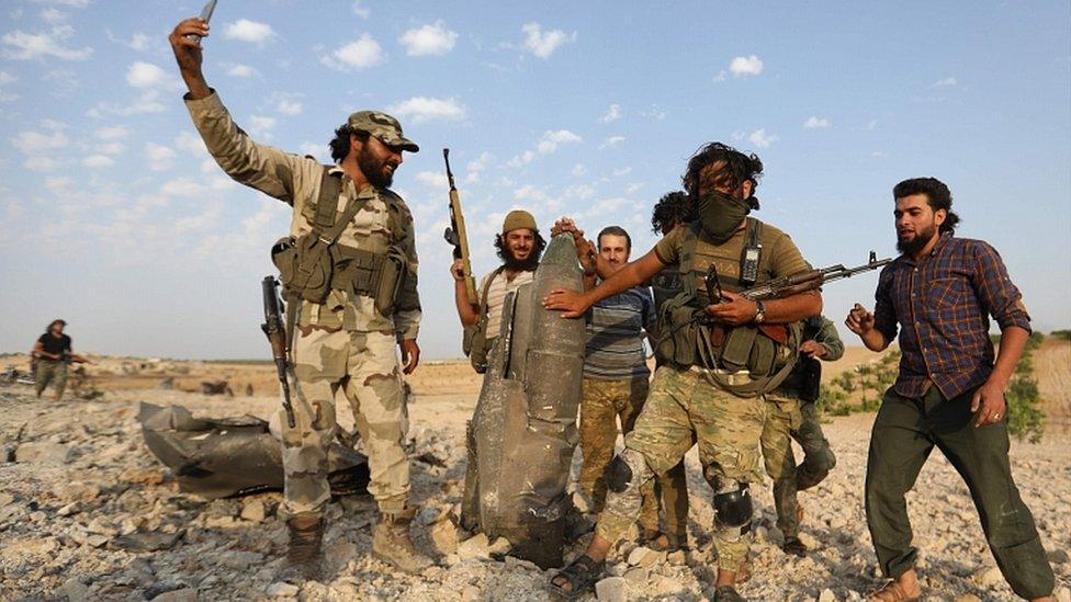 Rebel fighters pose for a picture with the remains of a downed warplane in the south of Idlib province on August 14, 2019