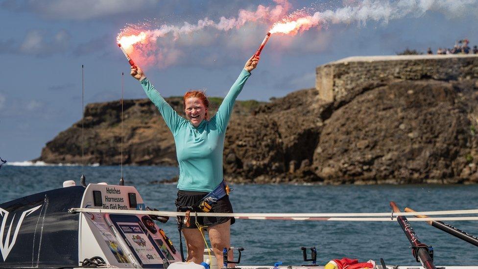 Leanne standing on her boat on arrival in Antigua, holding two red flares in the air in celebration.