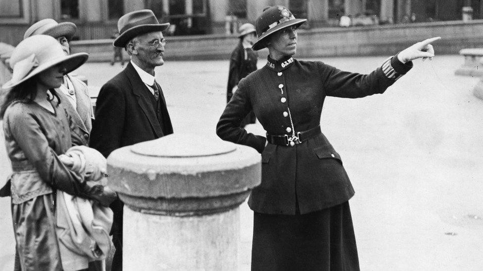 A female British Metropolitan Police officer points as she gives directions to a family of visitors from out of town, London, 1920s.