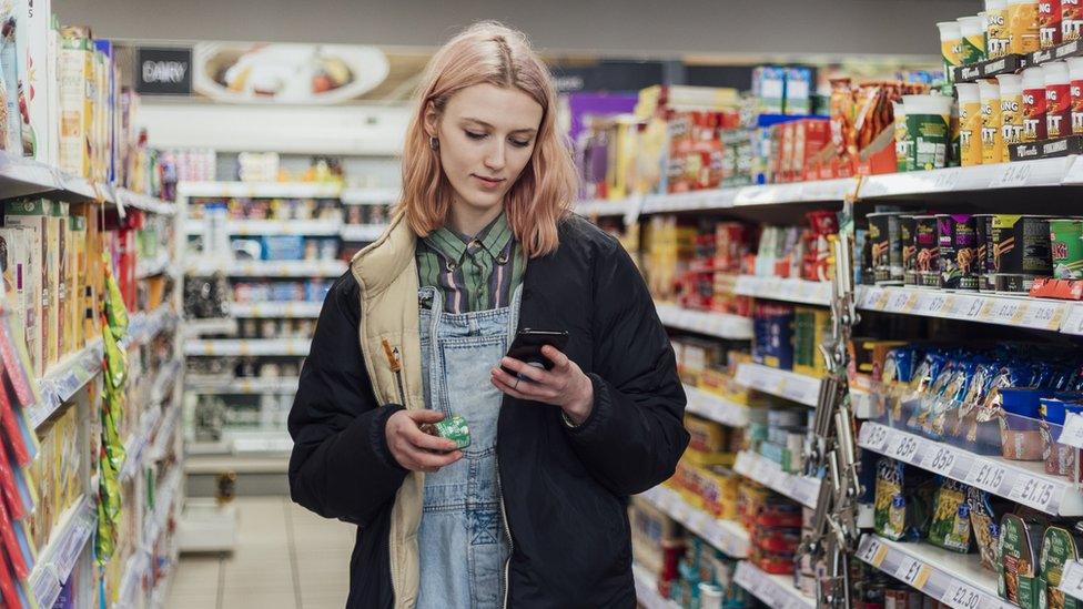 Woman looks at phone while holding a box of stock cubes in a grocery store