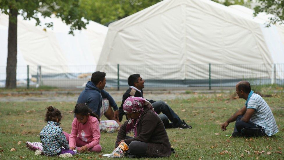 Migrants sit in the grass next to at an emergency, short-term shelter for migrants under construction on September 3, 2015 in Berlin, Germany