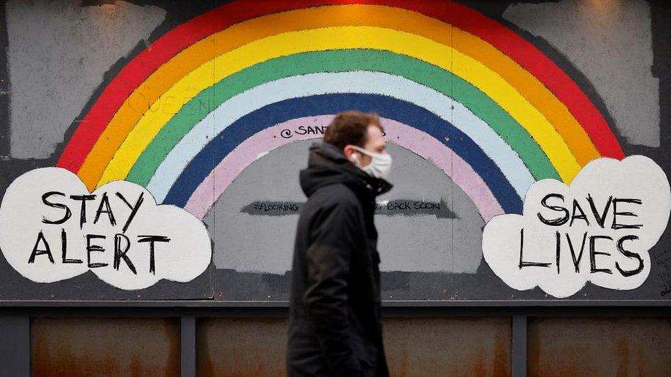 man in mask in front of rainbow sign stay alert save lives